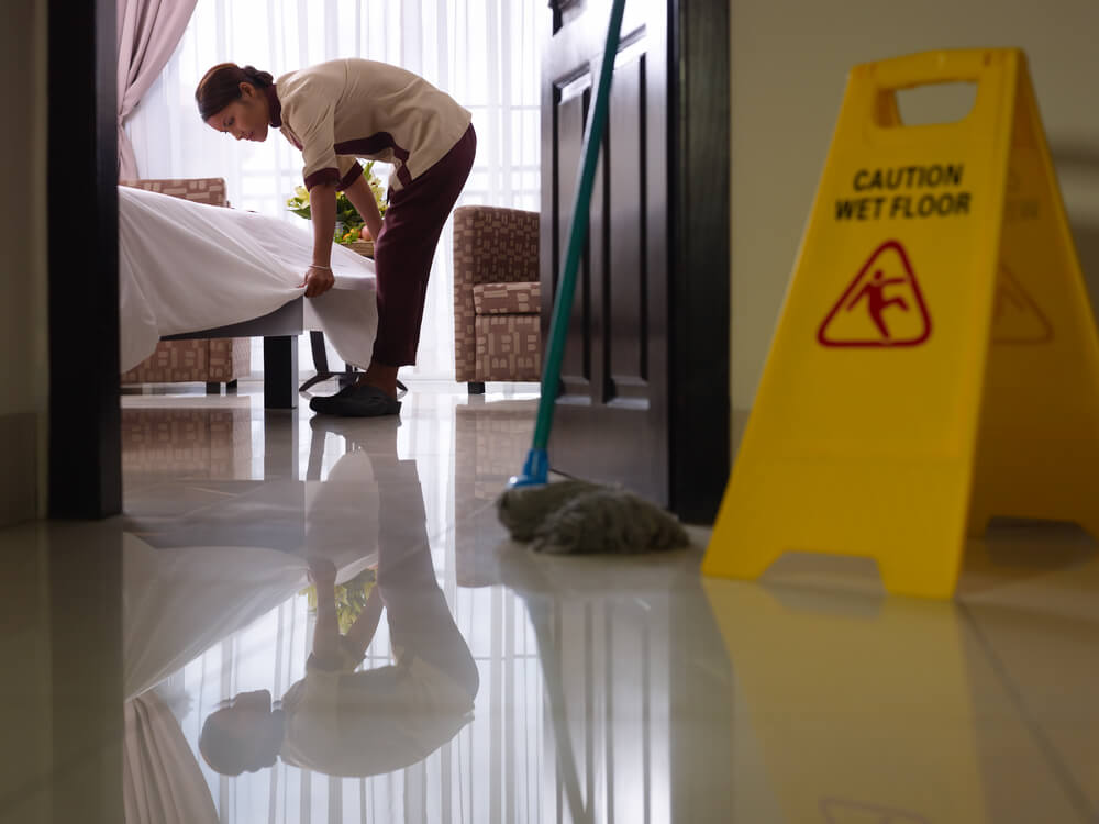 Asian maid tidying up bed and cleaning luxury hotel room with a caution wet floor sign Asian maid tidying up bed and cleaning luxury hotel room with a caution wet floor sign