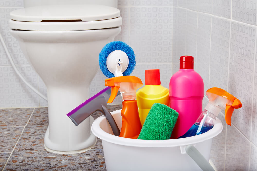 Close up view of House cleaning colorful products and tools in white bucket on tiled floor in toilet Close up view of House cleaning colorful products and tools in white bucket on tiled floor in toilet