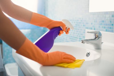 woman doing chores in bathroom at home, cleaning sink and faucet with spray detergent