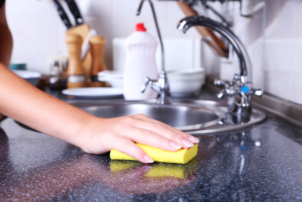 Using hands to clean kitchen with yellow sponge