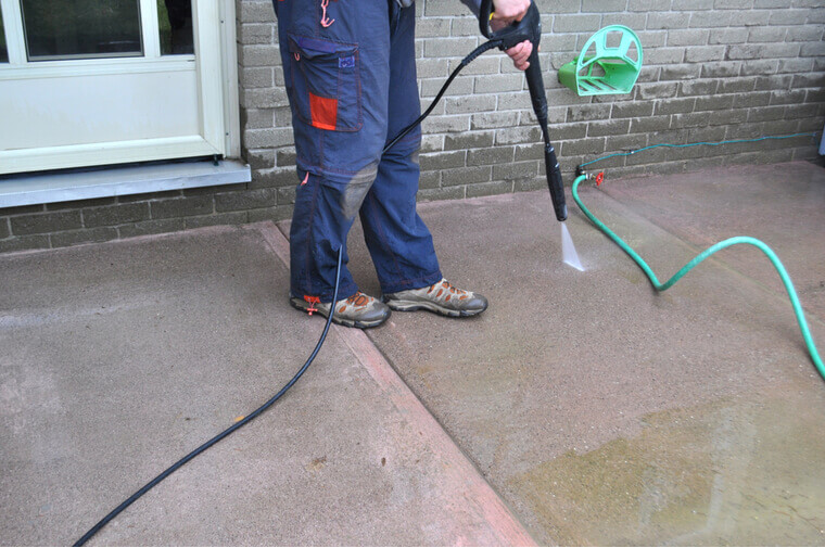 Spring yard work - a man cleaning a sidewalk with a pressure washer. Man cleaning a sidewalk with a pressure washer during spring yard and garden work