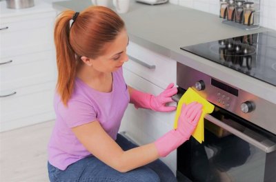 Woman cleaning modern oven with rag in kitchen