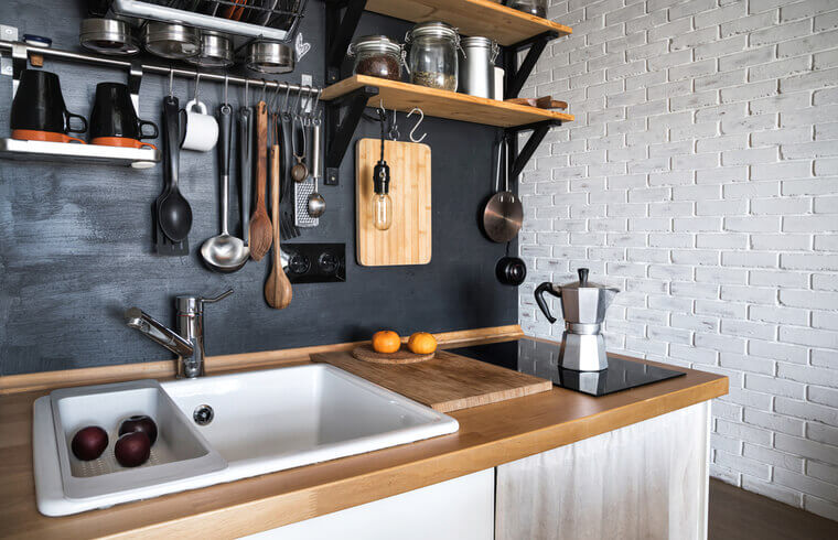 Design of a modern home kitchen in the attic and rustic style. Black wall with shelves, trays, jars, mugs, sink. In the background a wall of white brick