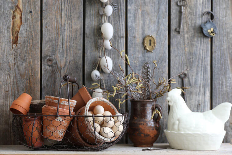 Easter Composition with Eggs Garland, Branch of Birch in old aged clay pitcher, weathered flower pots in metal wicker basket, authentic key, padlock, chicken, wooden background, Vintage, Rustic Style