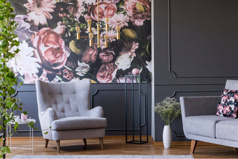 Grey armchair against flowers wallpaper in dark living room interior with sofa and plant Grey armchair against flowers wallpaper in dark living room interior with sofa and plant