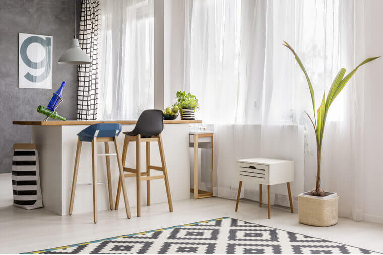Simple dining area with tall plant, wooden barstool, white kitchen island and poster on gray wall Simple dining area with tall plant, wooden barstool, white kitchen island and poster on gray wall