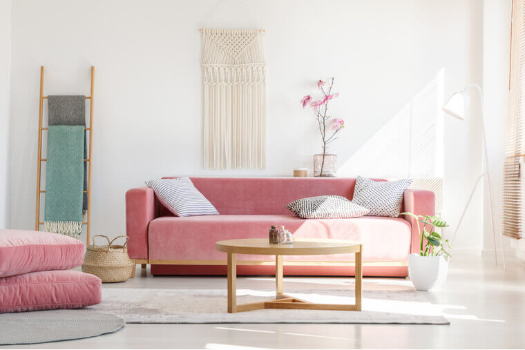 Cozy cushions and stylish textiles in a sunny, feminine living room interior with a pink, velvet sofa and a macrame on a white wall Cozy cushions and stylish textiles in a sunny, feminine living room interior with a pink, velvet sofa and a macrame on a white wall