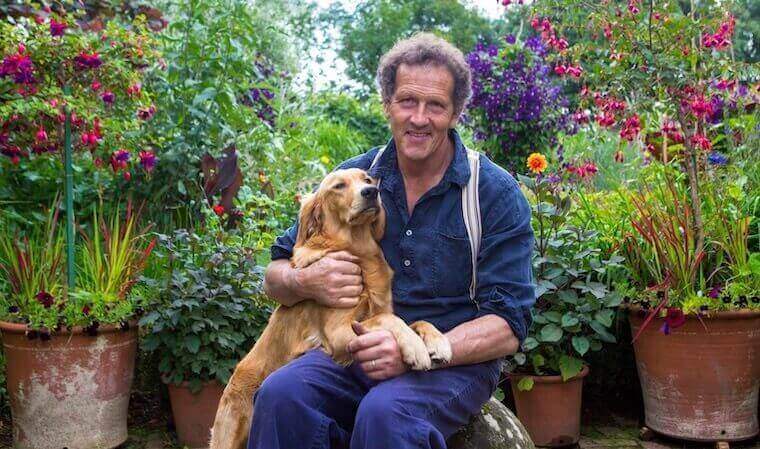 Monty Don holding his dog half on his lap while in a garden