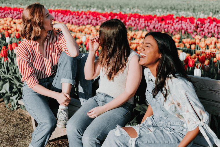 three happy women sitting in a bench next to a tulip garden