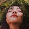 woman with her eyes closed near a fern