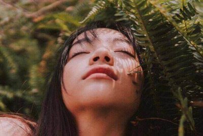woman with her eyes closed near a fern