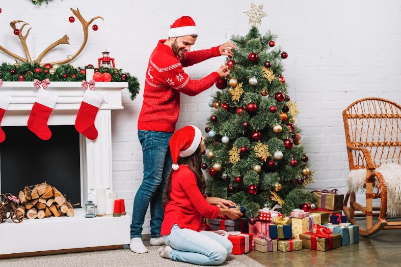 Guy and lady decorating christmas tree with baubles beside their fireplace Guy and lady decorating christmas tree with baubles beside their fireplace